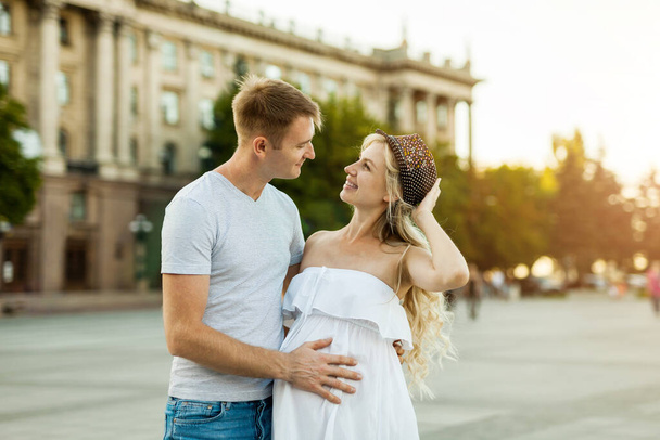 Atractive pregnant couple together in the city square. Beautiful pregnant woman and her boyfriend in the city - Foto, Imagen