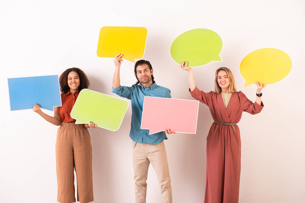 Happy intercultural friends in casualwear holding colorful blank paper speech bubbles where you can write your notes or posts - Photo, Image