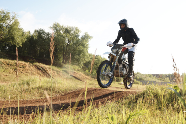 Ekstremalny człowiek w stroju ochronnym jest w powietrzu podczas jazdy na motocyklu na wzgórzach w konkurencji - Zdjęcie, obraz