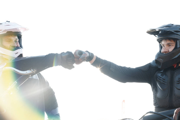 Команда профессиональных мотоциклистов в шлемах делает первый удар кулаком, приветствуя друг друга перед гонкой - Фото, изображение