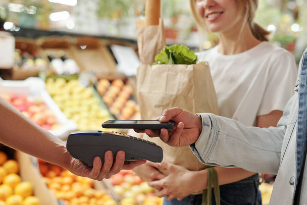 Detailní záběr mladých párů platících za čerstvé produkty s chytrým telefonem na trhu s ekologickými potravinami - Fotografie, Obrázek