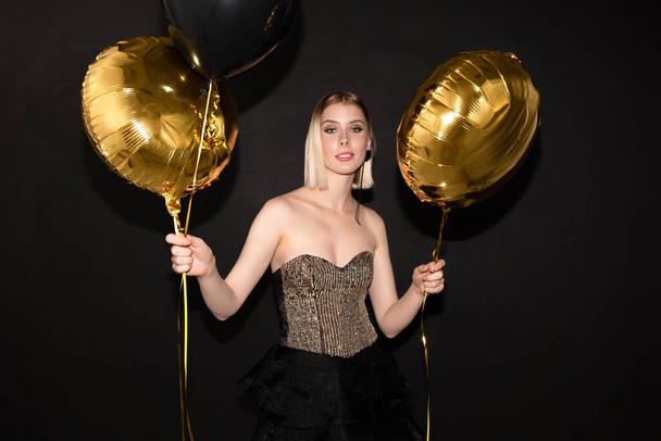Szczęśliwa młoda elegancka kobieta ze złotym kolorze balonów korzystających z uroczystości urodzin lub innej okazji przed kamerą - Zdjęcie, obraz