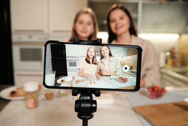 Екран смартфона під час живого майстер-класу домашньої кухні, де дві молоді жінки готують домашню айсберг на кухні
 - Фото, зображення