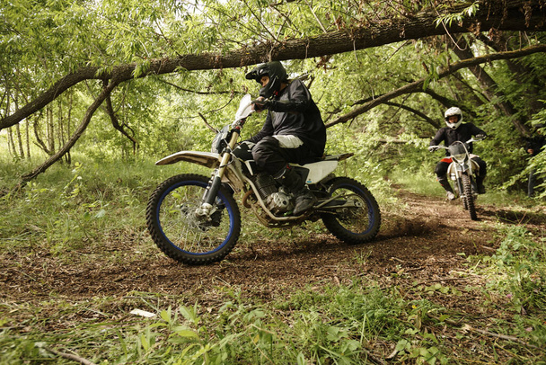 Orman engellerini aşmak için zorlu bir yolda motosiklet süren kasklı aşırı adamlar. - Fotoğraf, Görsel