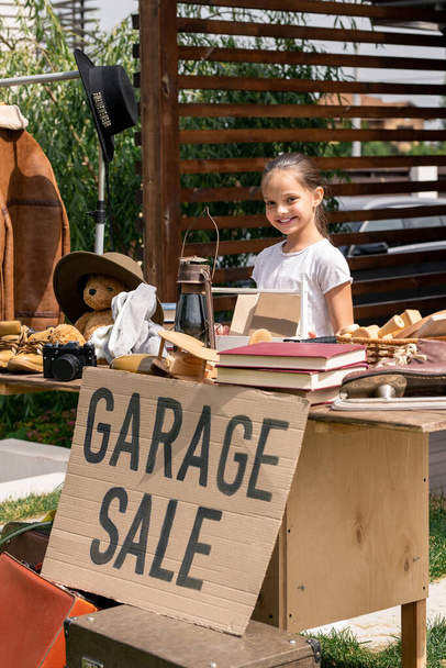 Portrait de petit vendeur souriant debout à la table avec panneau de vente de garage dans la cour arrière - Photo, image