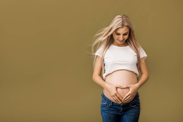 Close up of pregnant woman touching her belly on beige background. Pregnancy, maternity, preparation and expectation concept - Photo, image