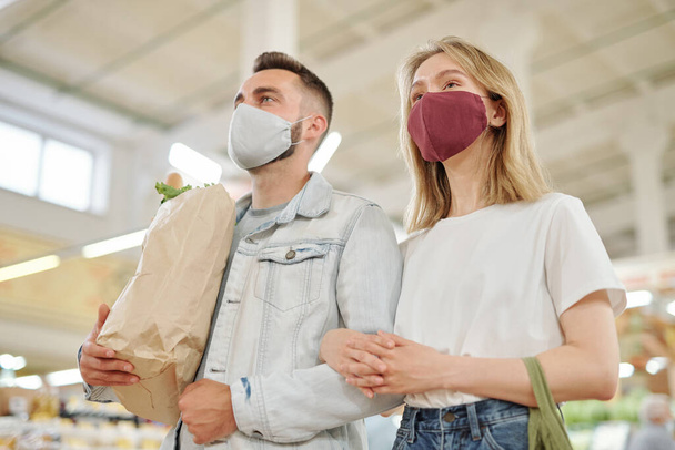 Poniżej widok młodej pary w maskach twarzy spacerując razem po rynku rolników podczas koronawirusu i kupując żywność - Zdjęcie, obraz