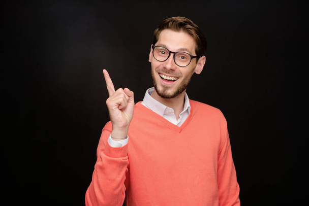 Portrait of cheerful smart young man with beard pointing finger up while having brilliant idea, isolated background - Photo, Image
