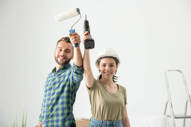 Portret pozytywnej młodej pary podnoszącej narzędzia przebudowy, gotowej do naprawy w nowym mieszkaniu - Zdjęcie, obraz