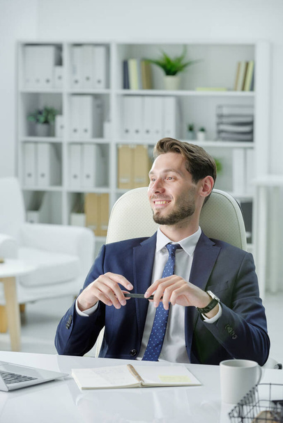 Un bell'uomo d'affari sorridente con la barba seduta alla scrivania e che ascolta il partner d'affari mentre lo incontra in ufficio - Foto, immagini