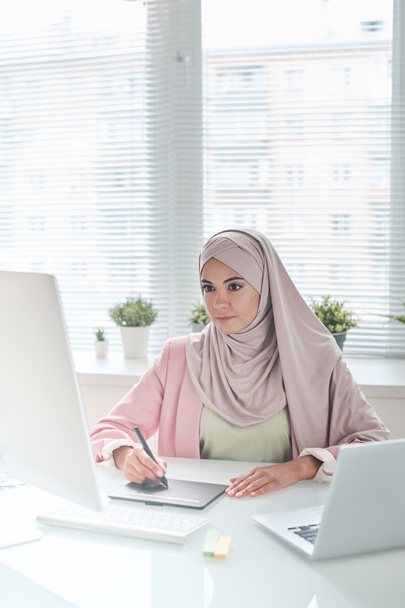 Content contemplative young Muslim businesswoman in pink hijab leaning on wall outdoors and thinking of message - Photo, Image