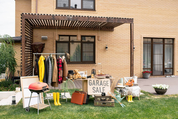 Гаражный знак продажи за столом с уникальными товарами на заднем дворе красивого кирпичного дома - Фото, изображение