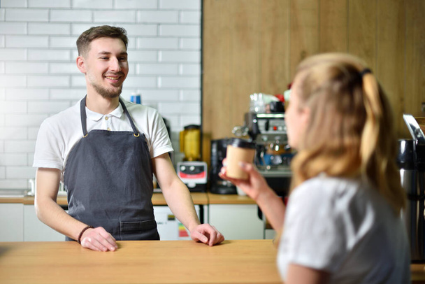 A young girl buys coffee in a coffee shop and talks with the bartender. Small business and communication concept - Photo, Image