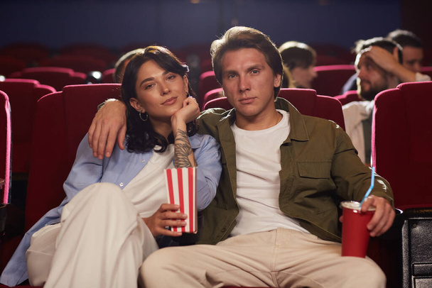 Портрет любящей молодой пары в кино, смотрящей кино и держащей попкорн, наслаждаясь романтическим свиданием - Фото, изображение