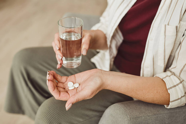 Warm toned close up of unrecognizable woman holding pills and glass of water, medicine and recovery treatment, copy space - Фото, зображення