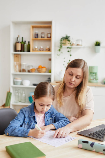 Vertical portrait of caring adult woman helping girl doing homework or studying at home while sitting at desk in cozy interior, copy space - Photo, image