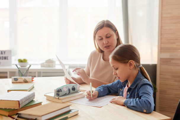 Портрет милої маленької дівчинки, що пише тест під час навчання вдома з матір'ю або вчителем, що допомагає їй, копіювати простір
 - Фото, зображення