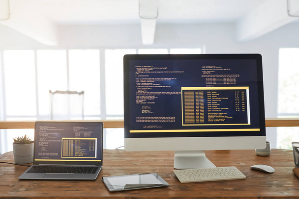 Vista frontal imagem de fundo de dois computadores com código de programação na tela no interior do escritório em casa mínimo com acentos de madeira, espaço de cópia - Foto, Imagem