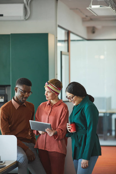 Vertical portrait of three contemporary business people discussing work in office, focus on young woman holding tablet and talking to colleagues, copy space - Foto, imagen