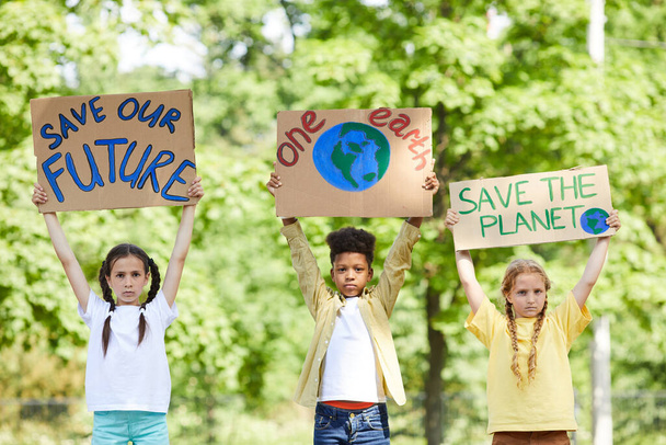 Cintura para cima retrato de três crianças segurando sinais com SAVE PLANET SAVE FUTURE enquanto protestando pela natureza ao ar livre, espaço de cópia - Foto, Imagem