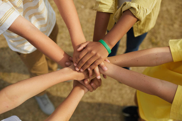 Vue de dessus en gros plan sur un groupe multi-ethnique d'enfants qui empilent leurs mains en cercle à l'extérieur, concept d'amitié et d'unité - Photo, image