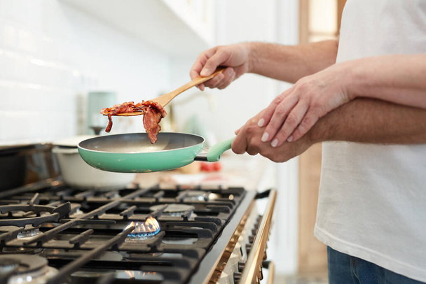 Close up of unrecognizable mature couple cooking breakfast together in home kitchen with focus on hands holding frying pan, copy space - Foto, Bild