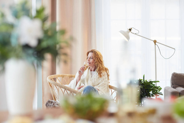 Portrait grand angle d'une élégante femme mûre appréciant le champagne tout en se prélassant à la maison et en détournant les yeux pensivement, copiez l'espace - Photo, image