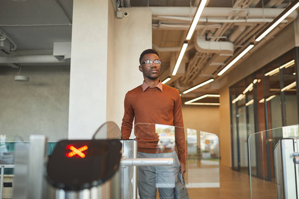 Porträt eines jungen afroamerikanischen Mannes, der beim Passieren eines automatisierten Tores den Personalausweis streift, um in ein Bürogebäude oder ein College zu gelangen, Kopierraum - Foto, Bild