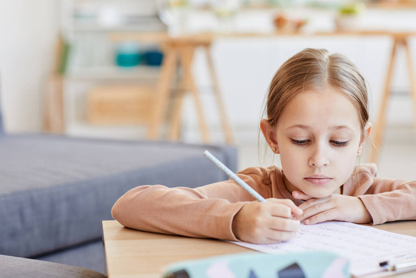 Close up retrato de menina loira bonito fazendo lição de casa de teste enquanto estuda em casa no interior acolhedor, espaço de cópia - Foto, Imagem