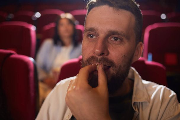 Head and shoulders portrait of mature man eating popcorn in cinema while enjoying movie alone, copy space - Фото, изображение