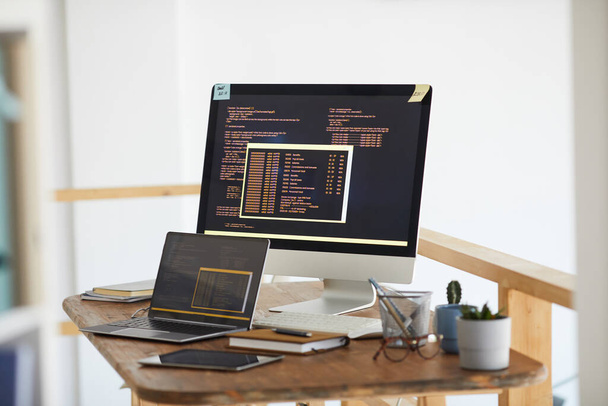 Obraz tła czarno-pomarańczowego kodu programowania na ekranie komputera i urządzeń cyfrowych w nowoczesnym białym wnętrzu biura, przestrzeń do kopiowania - Zdjęcie, obraz