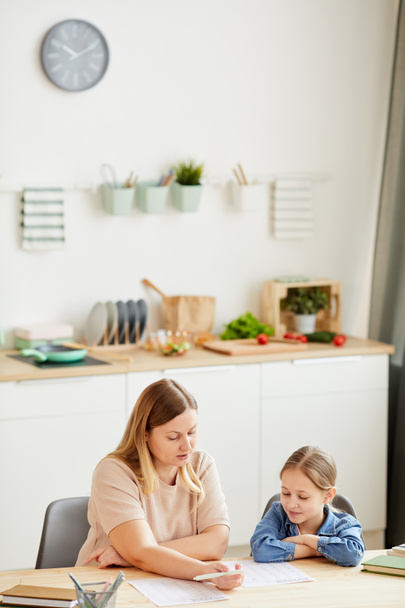 Vertikal warmfarbiges Porträt einer fürsorglichen Mutter, die ihrer Tochter bei den Hausaufgaben hilft und zu Hause im gemütlichen Interieur studiert, Kopierraum - Foto, Bild
