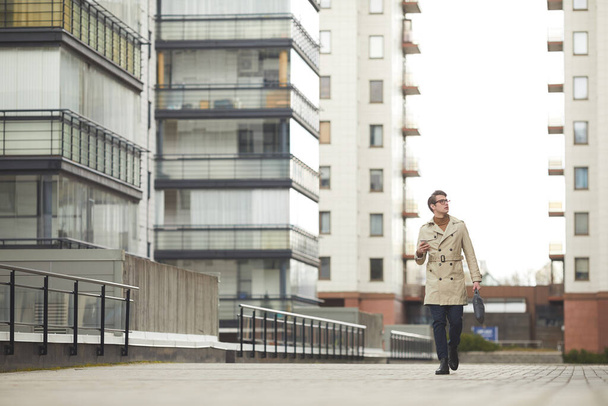 Retrato de gran angular del joven empresario moderno con gabardina que camina hacia la cámara mientras viaja al trabajo en el entorno urbano de la ciudad, espacio de copia - Foto, imagen