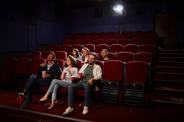 Широкий угол обзора группы друзей, смотрящих кино в кинотеатре, наслаждаясь частным просмотром в пустом зале, копировальное пространство - Фото, изображение