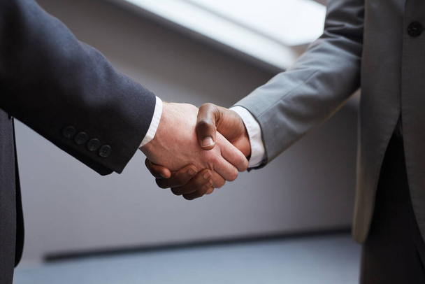 Close up of unrecognizable successful businessman shaking hands with African-American partner after closing deal, minimal background in grey tones, copy space - Photo, Image