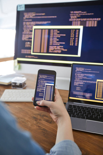 Vertikální zblízka ženské ruky držící smartphone s kódem na obrazovce při práci na stole v kanceláři, ženská IT vývojářská koncepce, kopírovací prostor - Fotografie, Obrázek