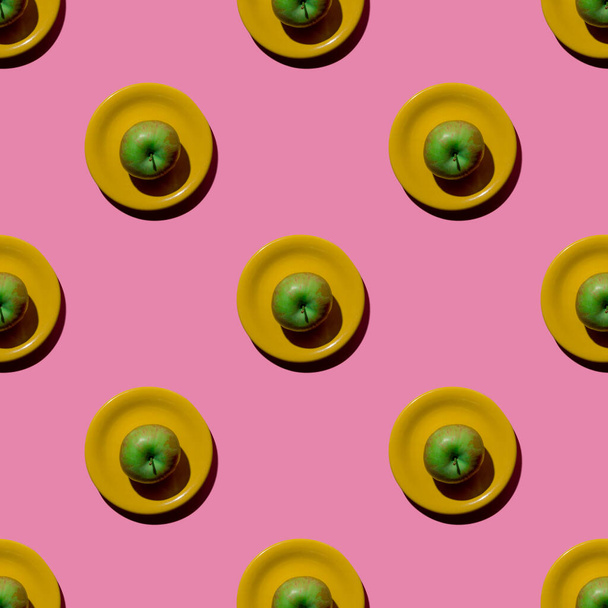 Fresh green apple on yellow saucer on pink background. Seamless pattern. Top view. Flatly. Hard light. - 写真・画像