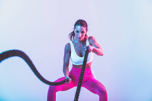 Fit woman training hard with ropes. Girl making exercizes in the gym. Concept about bodybuilding and lifestyle - Foto, Imagem