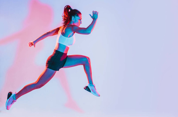 Beautiful fit woman making sport and running. Studio gel lighting - Zdjęcie, obraz