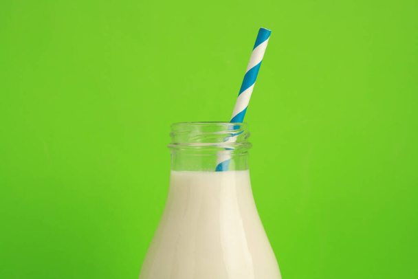 A closeup shot of glass bottle of milk with paper straw on green background - Photo, image