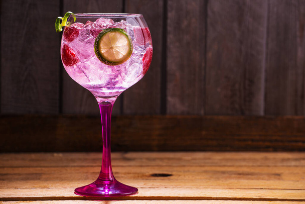 A closeup shot of a fresh cold cocktail with ice cubes and a slice of lime on a wooden surface - 写真・画像