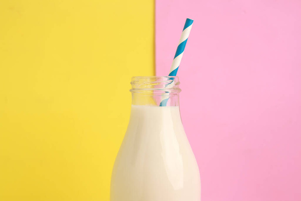 A closeup shot of milk in a glass bottle against a pink and yellow background - Photo, image
