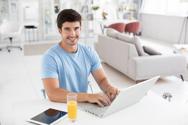 Happy smiling man works on his laptop at home. Cheerful freelance, distance job. - Valokuva, kuva