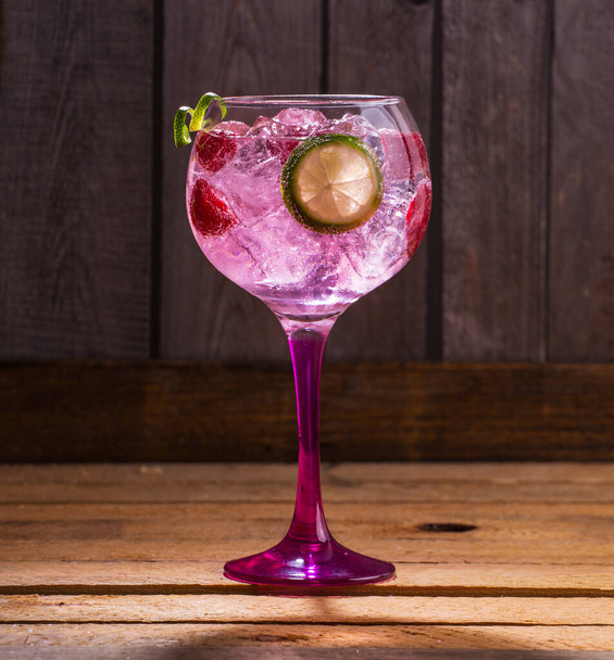 A closeup shot of gin tonic with raspberries and lime on a wooden table - Fotoğraf, Görsel