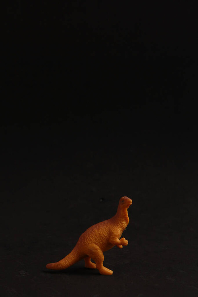 A vertical closeup shot of a dinosaur-shaped rubber toy on a black background - Fotó, kép