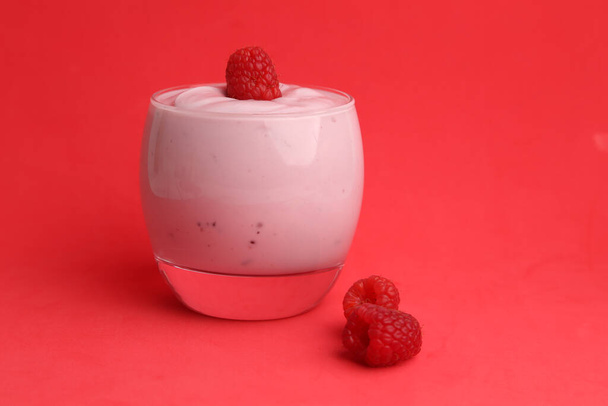 A closeup shot of a delicious raspberry yogurt on a red background - Фото, зображення