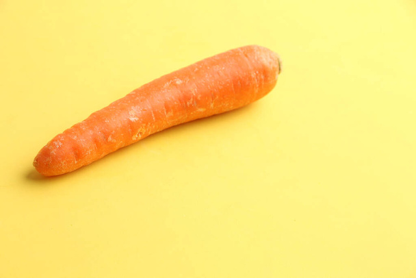 A closeup shot of a fresh carrot isolated on yellow background - Φωτογραφία, εικόνα