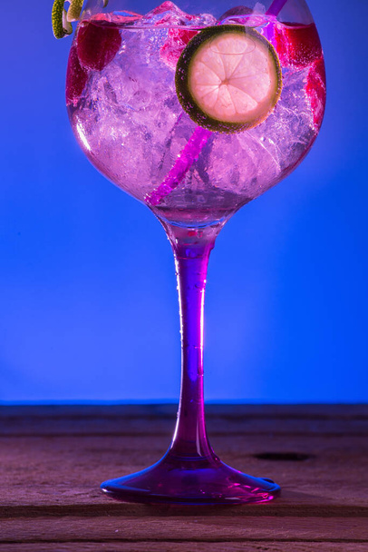 A vertical shot of a glass of cocktail with fresh lemon and berries on a wooden surface - Фото, изображение
