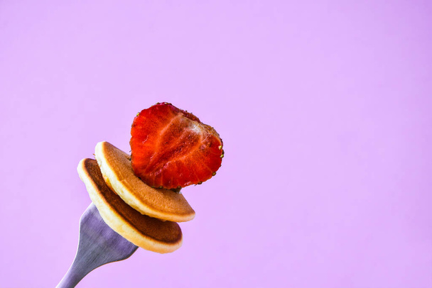 Selective focus on fork with tiny pancakes and strawberry. Pancake porridge, mini pancakes cereal in a bowl. Trendy food. Copy space for text - Photo, Image
