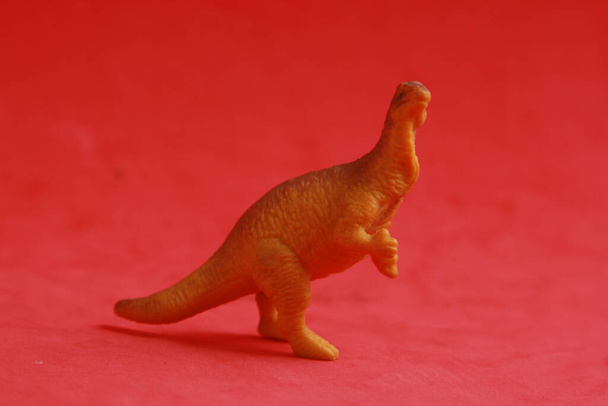 A closeup shot of a dinosaur figurine isolated on a red background - Fotó, kép